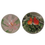 Conjunto de 2 pesos de papel em vidro artístico (art glass paperweight) decorado internamente com flores coloridas. A)  Apresenta padrão floral circular focado em uma peônia rosa, com folhas verdes suaves ao fundo. B) Apresenta pétalas em tons vibrantes de vermelho e laranja envoltas por uma base de folhagens verdes.