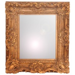 Espelho de parede decorativo com moldura clássica de estilo barroco, apresentando formato retangular e um acabamento ornamentado em tom dourado envelhecido. A moldura robusta é repleta de detalhes em relevo, como volutas e arabescos.