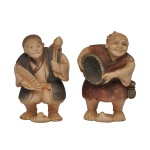 JAPÃO, Conjunto de 2 Netsuke, em marfim policromado, representando A) Um personagem com um leque (sensu) em uma das mãos e um bastão ou baqueta na outra, em uma pose expressiva e dinâmica. B) Um músico ou artista segurando um pequeno tambor de mão tradicional, exibindo um sorriso alegre e detalhado. São pequenas figuras detalhadas feitas no formato tradicional de netsuke (peças decorativas usadas originalmente como fechos de bolsas no Japão tradicional) ou okimono (estatuetas para exibição). Tradicionalmente entalhadas em marfim ou madeira de buxo (boxwood), com detalhes realçados em nanquim escuro para dar profundidade às feições e vestimentas.