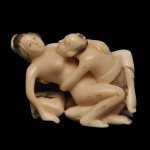 JAPÃO. Netsuke erótico, pertencente à tradição da arte sensual japonesa conhecida como shunga (literalmente "imagens de primavera"). Marfim esculpido, detalhado com incisões e pigmentos escuros nos cabelos e vestimentas. Embora muitas vezes ocultas devido à natureza íntima da cena, as peças de shunga netsuke celebravam o prazer, o humor e a sexualidade mútua sem os tabus ocidentais da época. Eram apreciadas por colecionadores e usadas tanto como amuletos de boa sorte quanto como itens de entretenimento privado entre adultos.