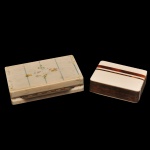 Conjunto de 2 peças em osso, sendo: A) Estojo articulado antigo, comumente utilizado no passado como porta-cigarros, porta-joias ou caixa de rapé (machetaria e marfim/osso). O modelo exibe delicados entalhes e gravuras florais em sua tampa superior e uma dobradiça de metal proeminente na lateral. B) Pequena caixa retangular com frisos rouge de fere acabamento quadrado com decorações lineares precisas.