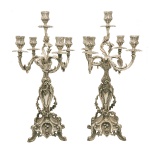 Par de candelabros para 5 velas em metal prateado, lavrados em estilo rococó e ornamentados por folhagens, reservas e concheados. Hastes retas e recortadas, sustentando braços recurvos centralizando ponteira com castiçal. Bobeches no formato de copos, apoiadas em adornos circulares. Bases quadrangulares abauladas e ornadas por volutas e leques, ladeadas por quinas sobre pés arqueados e revirados. 50 x 28 cm.