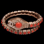 CHANEL. Bijoux - Bracelete de serpente vintage da Chanel criado por Karl Lagerfeld, pertencente à Coleção Cruise/Resort 2008. Estrutura articulada e ajustável que envolve o pulso simulando o formato de uma cobra. Metal em tom de ouro claro envelhecido, cravejado com cristais incolores (strass) e decorado com cabochões de resina que imitam pedra de coral vermelho. A cabeça da serpente traz uma grande pedra coral central ladeada pelo icônico logotipo de duplos CC entrelaçados cobertos de cristais. 7 cm. Peça nova, sem uso.