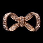 CHANEL. Bijoux - Broche em formato de laço da luxuosa marca Chanel. Formato de laço clássico e tridimensional, confeccionado em metal escovado com acabamento dourado. Totalmente cravejado com aplicação de cristais e stress brilhantes. Apresenta o icônico logotipo de duplo "C" entrelaçado da grife gravado sutilmente no lado inferior direito da fita. 6 x 3 cm. Peça nova, sem uso.