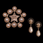 CHANEL. Bijoux  Conjunto de broche e par de brincos  Chanel em metal texturizado em tom ouro pálido, decorado com pérolas e uma estrela central de cristais (Strass). Lançado originalmente na coleção de Outono/Inverno de 2019 (gravado com o código da marca correspondente ao ano), este acessório de alta-costura traz o icônico logotipo de duplos "CC" posicionado exatamente no meio da estrela texturizada. Metal banhado a ouro pálido (blassgoldfarbenes Metall), resina imitando pérolas cabochão e cristais lapidados incolores. Uma moldura circular vazada cercada por 9 pérolas que orbitam uma estrela de cinco pontas, com o logotipo cravejado de pequenos cristais ao centro. PAR DE BRINCOS CHANEL CC Drop com pérola em formato de gota, caracterizado pelo icônico logotipo de duplo C entrelaçado em metal dourado e uma pérola sintética pendente. Sistema de tarraxa com base protetora transparente em formato de disco para melhor sustentação na orelha. No verso da peça, há a tradicional placa de assinatura oval gravada com as marcações "CHANEL B19 CC B Made in Italy".  4 x 4 cm. Peça nova, sem uso.