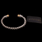 GIVENCHY, Bijoux  Bracelete vintage estilo cabo torcido, acompanhado por uma etiqueta original da renomada grife francesa Givenchy. Estrutura aberta (cuff) com corpo em formato de corda ou cabo de aço torcido oxidado. Estilo bicolor (two-tone), apresentando detalhes prateados e ponteiras esféricas douradas polidas nas extremidades. Inspirada no clássico design de alta joalheria em cabo, combinando sofisticação urbana com um toque industrial vintage. 8 cm. Peça nova, sem uso.