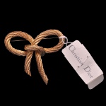 DIOR, Bijoux  Broche vintage da prestigiada marca Christian Dior, desenhado em formato de laço com textura que imita uma corda retorcida. Fabricado originalmente entre as décadas de 1970 e 1980, este modelo clássico possui acabamento folheado a ouro de alta qualidade.  Formato de laço entrelaçado (Rope Bow). 5 x 5 cm.