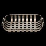 Cesta de pão ou fruteira vintage em metal espessurado a prata, provavelmente fabricada pela renomada marca francesa Christofle. Estrutura trançada feita com tiras planas de metal prateado, imitando o padrão de uma cesta de vime tradicional. Acabamento superior possui um cordão torcido em relevo que contorna toda a extensão da peça e duas alças fixas nas extremidades laterais, revestidas com detalhe em madeira escura (provavelmente ebanizada)