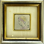 Pequena gravura artística italiana em prata esterlina 925, com retrato em relevo de jovem mulher no estilo Art Déco, dec. 1970, med. arte 4X4cm com moldura em madeira pintada com prata e proteção de vidro med. 11X11cm.  