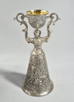 Antiga taça de casamento: "WAGER CUP" ou Jungfrauenbecher, em metal folheado a prata e interior em vermeil. Med. 21 cm; tradicionalmente composta por duas taças simultâneas: a menor em cima e outra na saia da figura. Historicamente, as taças eram usadas em festas e banquetes de casamento. O noivo bebia da taça maior, com a saia para cima, e a noiva bebia da taça menor, com a parte superior basculante. O desafio é esvaziar os dois copos simultaneamente sem derramar uma gota. VER OUTRAS --- https://www.metmuseum.org/art/collection/search/193559 ----https://www.ifranks.com/silverware/L4292-silver-wager-cups