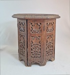 MARROCOS - Mesa de base oitavada articulada, em madeira entalhada e patinada em tom escuro. Formada por oito painéis dobráveis com entalhe vazado de folhagens de parreiras. Tampo octogonal com mesmo padrão floral em relevo e borda recortada. Alt. 40 cm e diam. 40 cm.