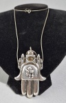 Joalheria Frank Meisler - Colar e grande pingente "HAMSA HAI" em prata de lei 925. Falta a pedra central e o grampo para broche. Med. Descrição do objeto: O topo retrata a silhueta das muralhas de Jerusalém com um olho protetor contra o mau-olhado, enquanto o centro da palma exibe o símbolo hebraico "Hai" (que significa "vida")  --- Ver valores:  https://frank-meisler.com/product/hamsa-hai/  ---- https://frank-meisler.com/about-2/