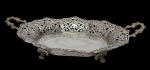 Antiga bandeja sextavada em metal espessurado a prata, com corpo vazado em delicado trabalho rendilhado, bordas recortadas e alças laterais ornamentadas em relevo. Apresenta fundo com gravação floral estilizada, conferindo elegância ao conjunto. Peça de feição clássica, adequada para compor serviços de mesa ou decoração. Medidas: 41 x 26,5 x 9 cm.