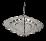 Antiga fruteira em metal espessurado a prata, com corpo em formato floral de bordas onduladas, decorada com delicadas gravações ornamentais e centro em relevo. Possui alça superior arqueada com haste torcida. Medidas: 14 x 21 x 17,5 cm.
