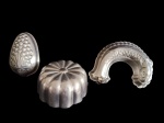 Lote contendo três formas em metal espessurado a prata, sendo uma em formato de cacho de uvas com decoração em relevo, uma circular com gomos em formato floral e outra em formato de peixe com escamas estilizadas. Medidas: 21 x 13 cm / 22 x 9,8 cm / 30 x 10 x 6 cm.