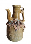 Jarra decorativa israelense em cerâmica vitrificada, com corpo cilíndrico, gargalo alongado e bico vertedor, apresentando alça lateral integrada. Decorada com aplicações florais em relevo na porção central e detalhes ornamentais incisos no corpo. Medidas: 39,5 x 21,5 cm.