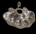 Antigo porta-ovos, produzido em metal espessurado a prata, com compartimentos individuais para ovos e suporte central para recipiente, apresentando desenho funcional de época. Medidas: 26 x 22 x 8,5 cm.