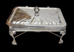 Antigo rechaud em metal espessurado a prata, com tampa articulada de decoração raiada, estrutura vazada e pés curvos estilizados, acompanhado de reservatório interno para aquecimento. Medidas: 38 x 25 x 22 cm.