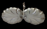 Imponente petisqueira de dois compartimentos, produzida em metal meridional espessurado a prata, com corpo em formato de folhas estilizadas, bordas rendilhadas vazadas e alça central ornamentada. Medidas: 37 x 19,5 x 16 cm.
