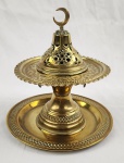Conjunto composto por recipiente com tampa vazada encimada por crescente islâmico, acompanhado de prato circular decorado. Peças em metal dourado com ornamentação em relevo e bordas trabalhadas. Medindo: 11 x 18 cm, 22 cm e 12 x 9,5 cm.