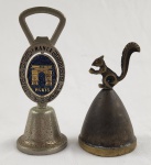 Duas campainhas de mesa em metal, sendo, um souvenir de Paris com acabamento em latão, corpo texturizado e alça em formato de abridor com emblema oval representando o Arco do Triunfo; a outra em tom bronzeado, com figura de esquilo esculpido no topo em posição sentada. Medindo.:12 cm e 10cm.