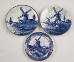 Três pequenos pratos decorativos holandeses em cerâmica Delft azul e branca, representando moinhos de vento em azul royal, verso com marca do fabricante. Medindo: 14cm e 12 cm