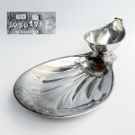 CHRISTOFLE, PARIS - Elegante e diferenciada petisqueira com molheira encaixada em metal com banho de prata da famosa fábrica de ourivesaria prateada para serviços de mesa de origem francesa. Base com ramos de trigo em relevo com dois pés e marca de manufatura no verso. Med 40 x 24 cm.