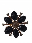 Anel confeccionado em metal de tonalidade dourada, com design inspirado em uma flor estilizada. A peça apresenta seis elementos ovais em acabamento preto brilhante, dispostos como pétalas ao redor de uma pedra central facetada em tom fumê. Aro 16.