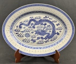 China. Travessa oval em porcelana chinesa, com decoração em policromia azul sobre fundo branco, apresentando motivo central de dragão e borda ornamentada com frisos geométricos em estilo oriental. Padrão Grão de Arroz. Medindo: 40,5 x 29,5 cm.