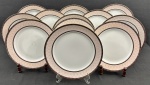 Schmidt. Doze pratos rasos em porcelana n acional padrão Gold, esmaltada na cor branca, com composição geométrica delicada em tons suaves. Borda ornamentada por uma faixa em rosa-claro com desenho em losangos entrelaçados, formando uma trama contínua e sutil. Essa faixa é emoldurada por frisos em marrom escuro, enriquecidos com pequenos detalhes dourados e filetes pontilhados. Manufatura no verso. Medindo: 28 cm.