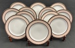Schmidt. Doze pratos para sobremesa em porcelana n acional padrão Gold, esmaltada na cor branca, com composição geométrica delicada em tons suaves. Borda ornamentada por uma faixa em rosa-claro com desenho em losangos entrelaçados, formando uma trama contínua e sutil. Essa faixa é emoldurada por frisos em marrom escuro, enriquecidos com pequenos detalhes dourados e filetes pontilhados. Manufatura no verso. Medindo: 19,5 cm.