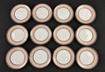Schmidt. Doze pratos para pão em porcelana n acional padrão Gold, esmaltada na cor branca, com composição geométrica delicada em tons suaves. Borda ornamentada por uma faixa em rosa-claro com desenho em losangos entrelaçados, formando uma trama contínua e sutil. Essa faixa é emoldurada por frisos em marrom escuro, enriquecidos com pequenos detalhes dourados e filetes pontilhados. Manufatura no verso. Medindo15  cm.