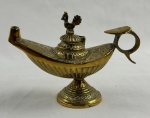 Lamparina decorativa em metal dourado, em formato oriental inspirado nas tradicionais lâmpadas de Aladim, com corpo ricamente ornado por gravações em relevo, tampa articulada e pegador em argola. Assentada sobre base pedestal. Medindo 10 x 14 cm.