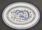 China. Travessa oval em porcelana chinesa, com decoração em policromia azul sobre fundo branco, apresentando motivo central de dragão e borda ornamentada com frisos geométricos em estilo oriental. Padrão Grão de Arroz. Medindo: 36 x 27 cm