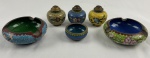 Lote contendo 6 peças em metal cloisonné, sendo 2 cinzeiros, 3 saleiros/pimenteiros com tampa perfurada e 1 pequeno recipiente, todos decorados com esmaltação policromada em vibrantes tons de azul, verde, amarelo e creme, apresentando motivos florais e arabescos orientais delimitados por finos filetes metálicos. Medindo de 2 x 4,5 cm a 3 x 8,5 cm.