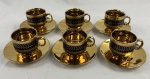 Conjunto contendo 6 xícaras de café e 6 pires em porcelana fina (Fine Porcelain) com acabamento esmaltado, com banho dourado em alto brilho. As xícaras apresentam uma faixa superior decorativa em tom escuro (preto) com padrão de escamas/colmeia em dourado. O interior das xícaras e o centro dos pires são inteiramente dourados. Acondicionado em sua caixa original.