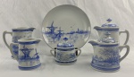 Conjunto para servir em estilo "Delft Blue. Inclui 01 bule de café, 01 bule de chá, 01 leiteira, 01 cremeira, 01 açucareiro com tampa e 01 prato de bolo/tortas. Porcelana vitrificada de fundo branco leitoso, ornamentação em azul cobalto sob o, apresentando paisagens típicas dos Países Baixos, incluindo moinhos de vento, embarcações a vela, igrejas e casarios. Bordas realçadas com filetes azuis.