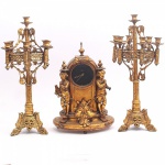 FRANÇA - Magnífico terno francês composto por relógio dito bim bam com caixa em metal finamente cinzelado e policromado, decoração adornada com esculturas representado musicistas, área inferior esculpida com rosto de figuras, e na área superior adornado com bilros e florões mostrador esmaltado, máquina em metal sem garantia de funcionamento e dois candelabros para sete velas com base finamente fenestrada e decorada com treliças, volutas e arabescos, coluna central decorada com flores e perolados, hastes recurvas sustentando argola com galeria geométrica vazada e bobeches em forma de flor, Atura do relógio: 50cm. Altura do Candelabro: 63cm - Não apresenta chave. Apresenta avaria na posta do relógio e um castiçal necessário ajuste em uma haste.