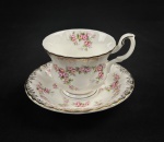 Xícara para chá com pires em porcelana esmaltada, marca Don Ton Mano, com decoração floral em tons de rosa sobre fundo branco, adornada por frisos dourados e borda recortada em estilo clássico.