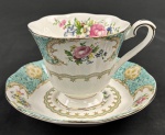 Xícara para chá com pires em porcelana esmaltada, da marca Don Ton Manor, com decoração floral policromada sobre fundo branco, apresentando reservas em tom turquesa com arabescos e ricos frisos dourados. Peças com bordas recortadas e acabamento de inspiração clássica europeia.