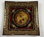 Prato ornamental de vidro com resina sintética moldada com acabamento esmaltado, formato quadrado. Apresenta fundo em tom vermelho-rubi, possui medalhão circular com estampa de cena de época retratando crianças, margeado por delicados ramalhetes florais nos cantos.