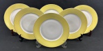 Mauá. Seis pratos rasos em porcelana esmaltada com borda amarela sobre fundo banco. Filetes em ouro. Manufatura no verso. Medindo: 23 cm.