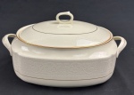 RC Bone China by Noritake, Japan. Terrina em porcelana esmaltada, em tom marfim, com bordas decoradas em relevo com arabescos e delicado friso em ouro na borda, com acabamento refinado e decoração em baixo-relevo. Medidas; 12 x 26 x 16 cm.
