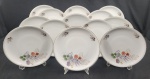Real. Treze pratos rasos em porcelana esmaltada, decorado com delicados motivos florais policromados sobre fundo branco e friso dourado nas bordas. Manufatura no verso. Medindo: 25 cm.