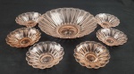 Sete peças em vidro na cor salmão, contendo 1 fruteira com acabamento moldado, corpo em formato circular com bordas caneladas e fundo decorado em relevo radial, acompanhada de 6 tigelas menores de mesmo padrão, peça maior 29 cm de diâmetro, bom estado de conservação. Medindo: 7 x 29 cm e 4 x 13,5 cm.