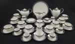 Conjunto para café e chá em porcelana Steatita, composto por 1 bule de café, 1 bule de chá, 1 leiteira, 1 açucareiro com tampa, 1 prato de bolo, 7 xícaras para café com respectivos pires e 12 xícaras para chá, em porcelana branca com friso prateado, marca da manufatura na base. Medindo; 17 x 25 x 15 cm, 19 x 24 cm, 13 x 17 cm, 9 x 16 x 11 cm, 7 x 15,5 cm e 27cm.