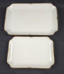 Hutschenreuther Hohenberg, Alemanha. Duas travessas em porcelana alemã esmaltada na cor branca, borda com rendilhado em preto sobre fundo dourado. Manufatura ao verso. Medindo:  24 x 35 e 31 x 45 cm