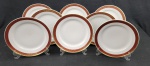 Oito pratos rasos em porcelana polonesa Karolina, na cor branca esmaltada, com abas em tom rubi decoradas por arabescos e folhagens em ouro, bordas filetadas. Medida: 24,5 cm. Apresenta marcas de desgaste na ornamentação em ouro.