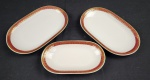 Três travessas em porcelana polonesa Karolina, na cor branca esmaltada, com abas em tom rubi decoradas por arabescos e folhagens em ouro, bordas filetadas. Apresenta marcas de desgaste na ornamentação em ouro.