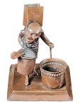 Grupo escultórico representando figura inspirada em Quasimodo, sustentando um cinzeiro, fosforeira e vaso para cigarros. Dito isto: é um conjunto para fumantes. 16 x 13 x 13 cm.